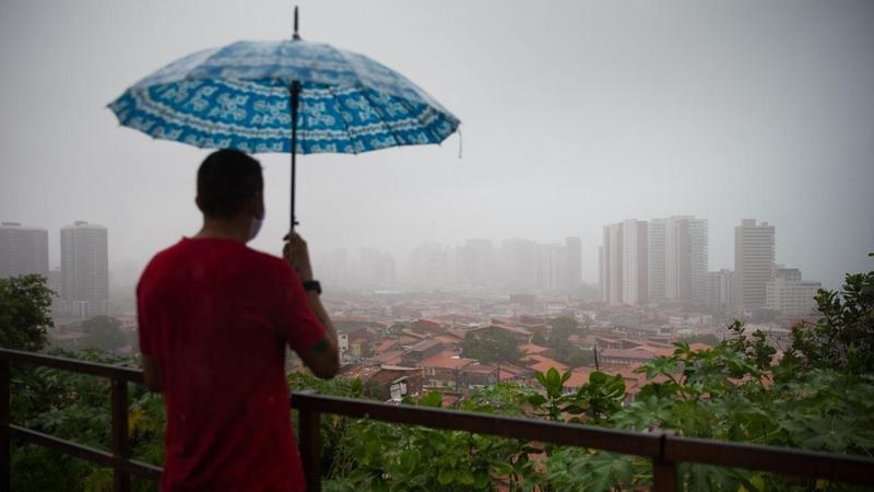 Imagem de um homem debaixo de um guarda-chuvas enquanto chove